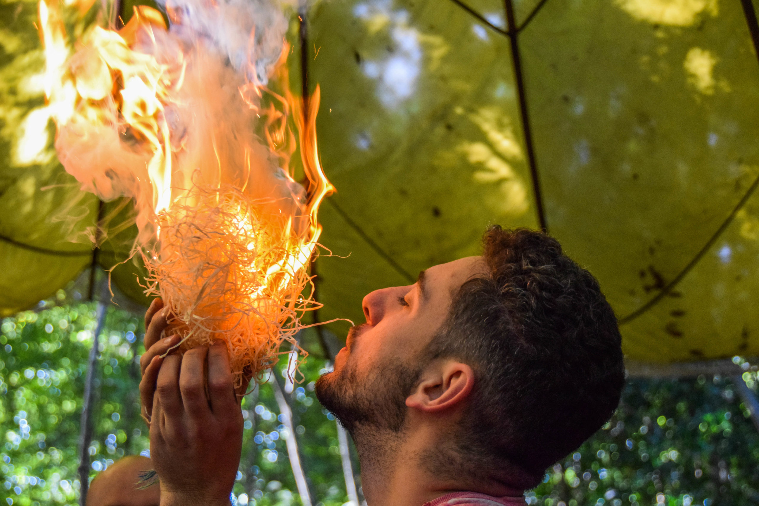 man blowing into a fire to give it oxygen