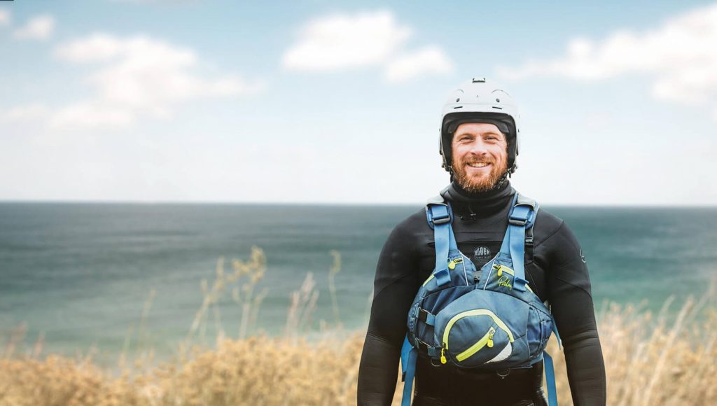 Man dressed in wetsuit with helmet standing in front of a sea view to illustrate the great reasons to work outdoors