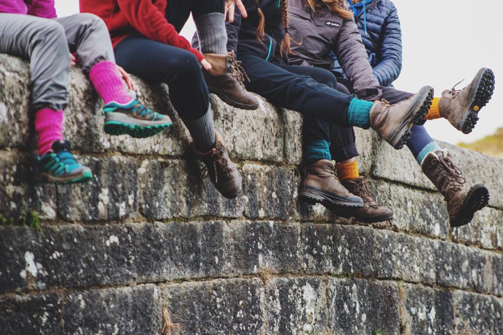 Five people sitting on wall wearing walking boots and trainers to illustrate various outdoor footwear options