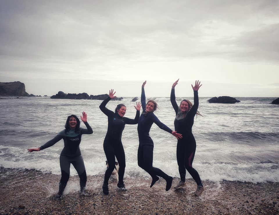 Four women jumping in the cold sea in wetsuits