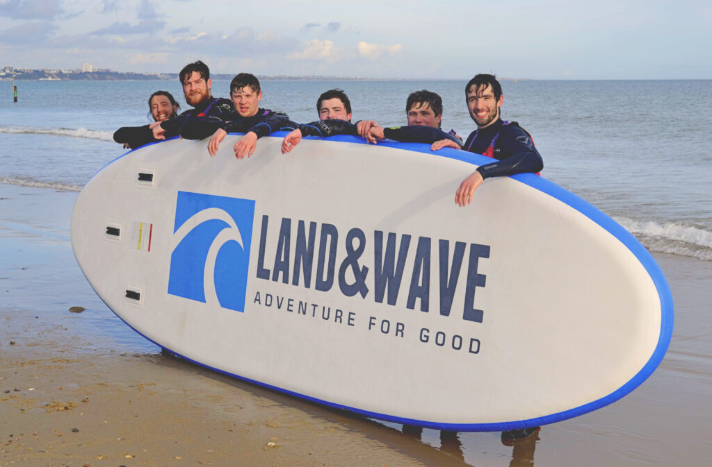 Six men holding up a Land & Wave Jumbo SUP in Sandbanks, Dorset