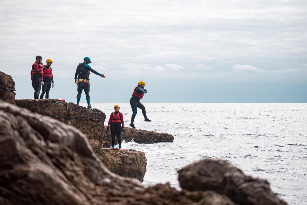 A group of people coasteering with a person jumping from a ledge into the sea. Completed.