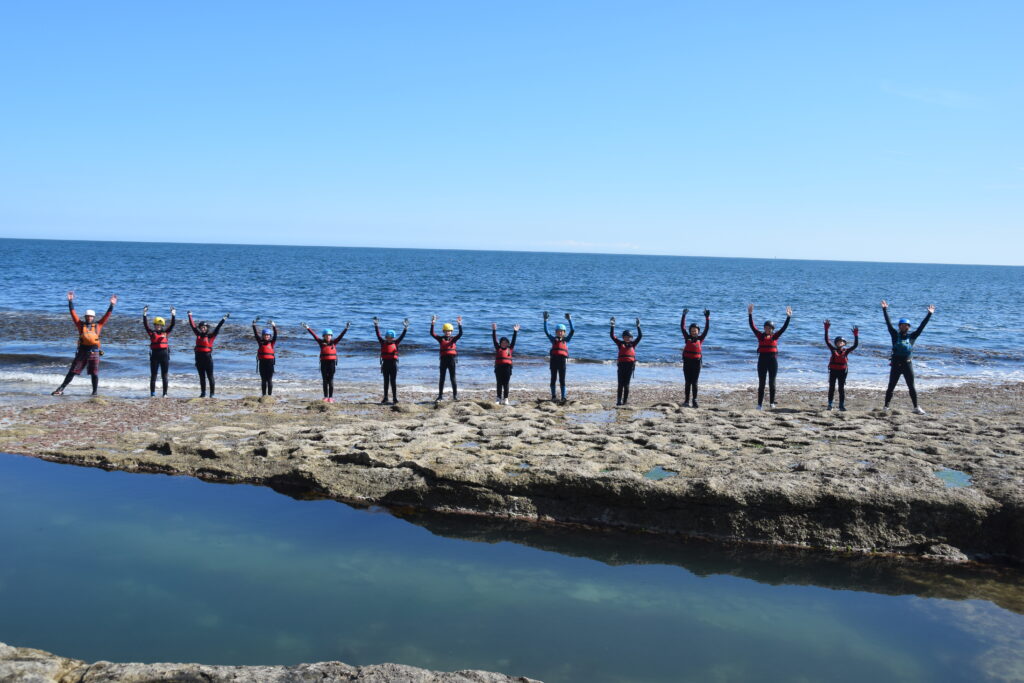 Outdoor Education Trip - A group of people with their arms in the air by the sea