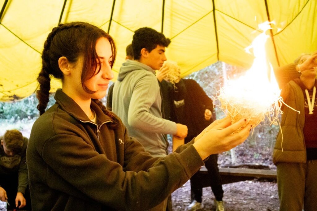 A Teenage Girl holds a flaming ball of kindling in the woods 