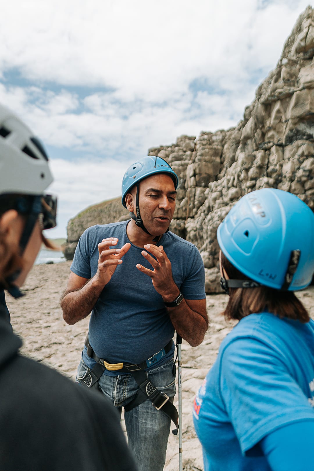 Amir Latif wears a blue climbing helmet and talks to two other climbers using his hands to gesticulate