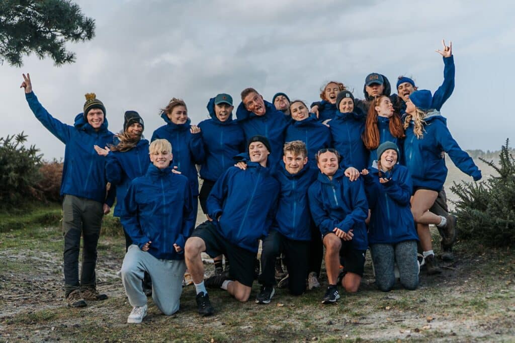 Group of 18 people. Men and women aged 18-27. All in blue lightweight waterproof jackets. Overcast sky in background. This is why you should come to an Open day