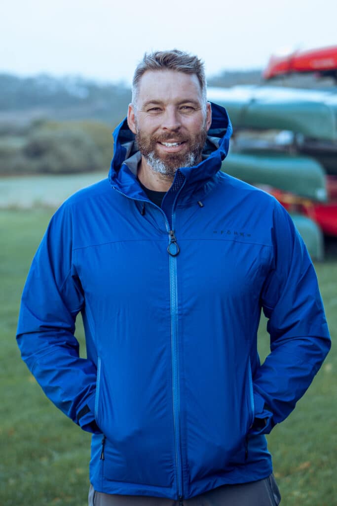 Outdoor Instructor Daniel Lees stands in front of canoes in the outdoors