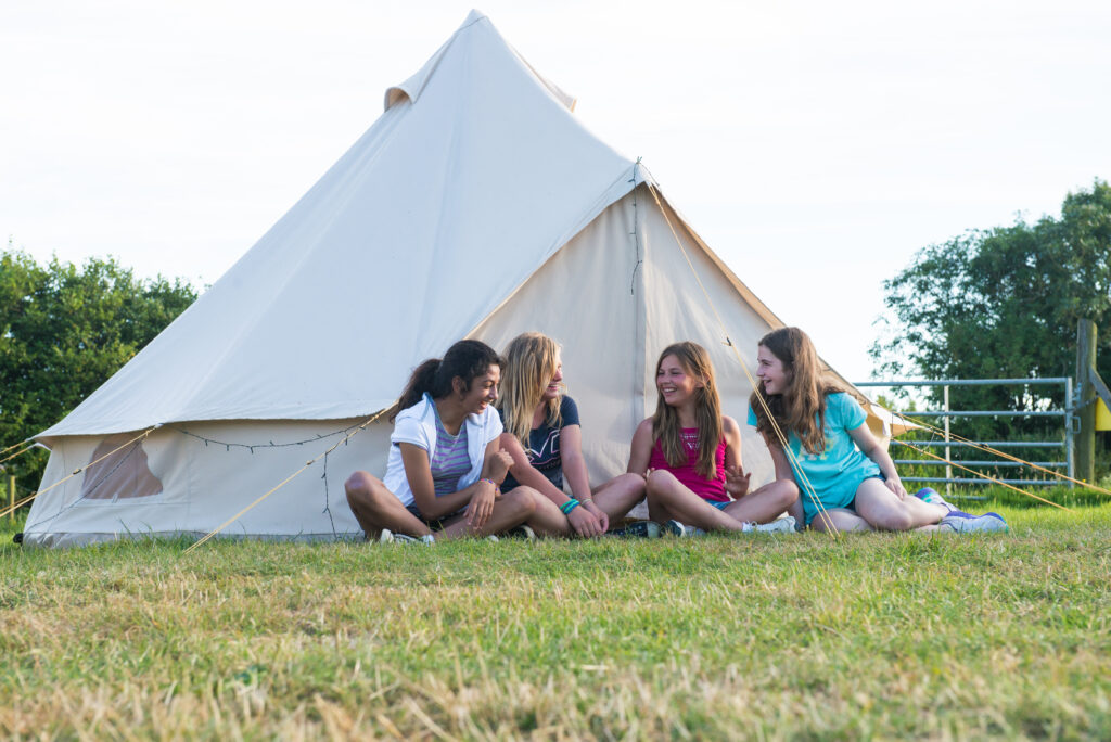 School girls sat infront of a bell tent in a green field