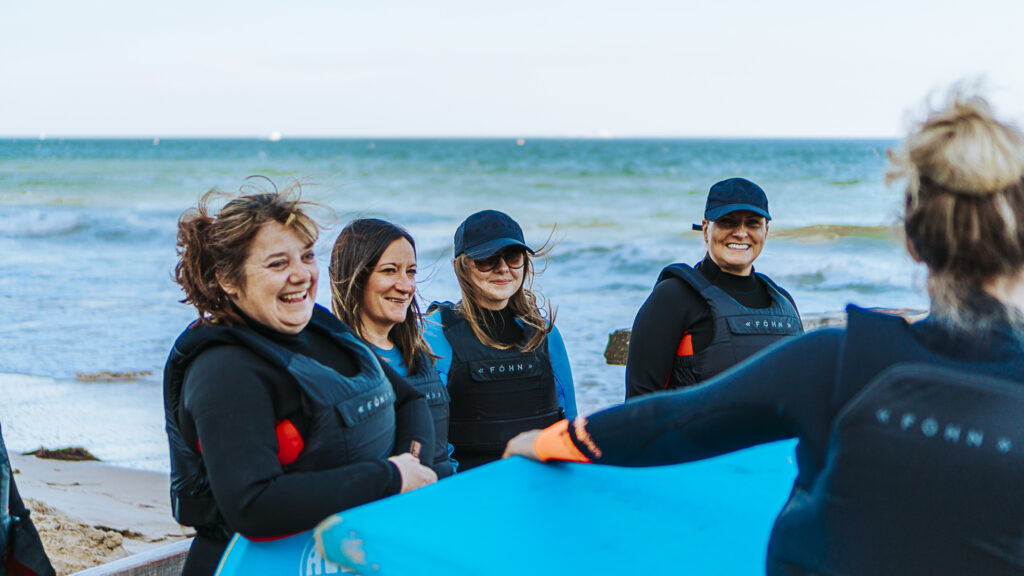 Smiling women at the beach in wetsuits and holding body boards